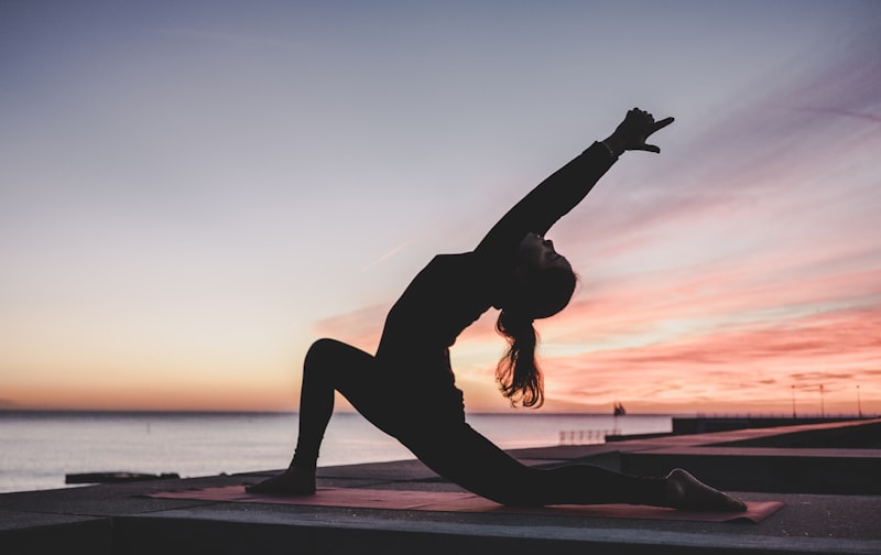 Person doing yoga stretches outdoors at sunset by the water